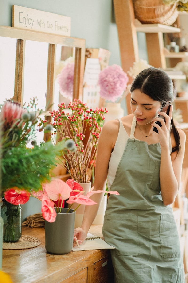 Female florist in apron having conversation on mobile phone to her small business management consultant.