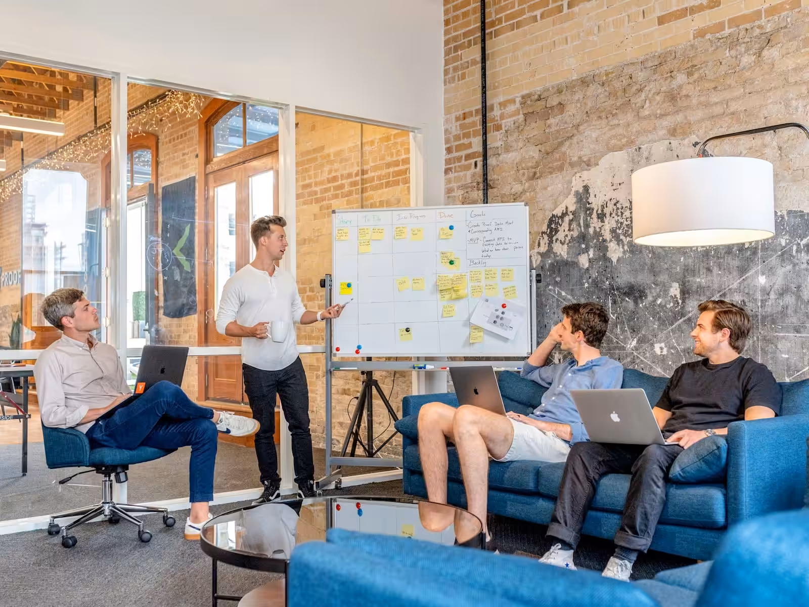 Three clients sitting while using laptops and watching male business consultant beside whiteboard. Small Business Management Consulting. Blaze Business & Legal Services