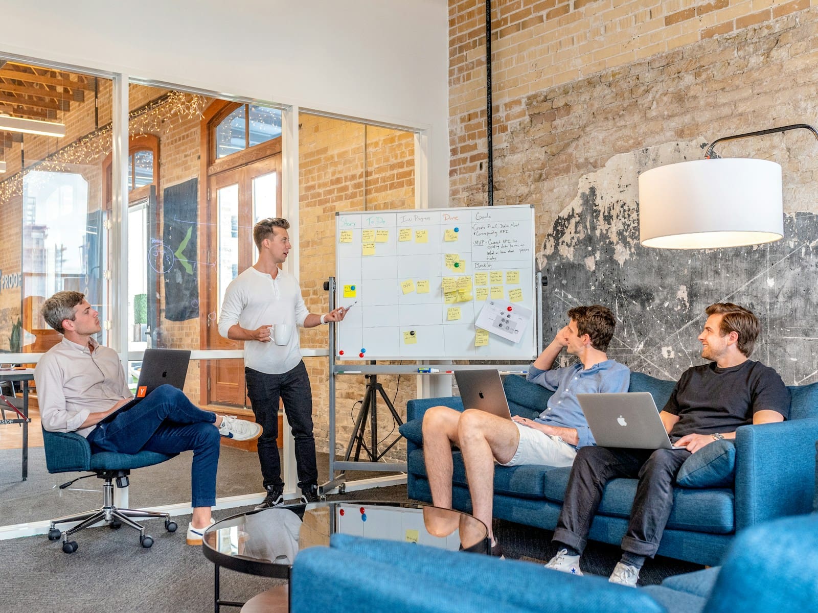 Three clients sitting while using laptops and watching male business consultant beside whiteboard. Small Business Management Consulting