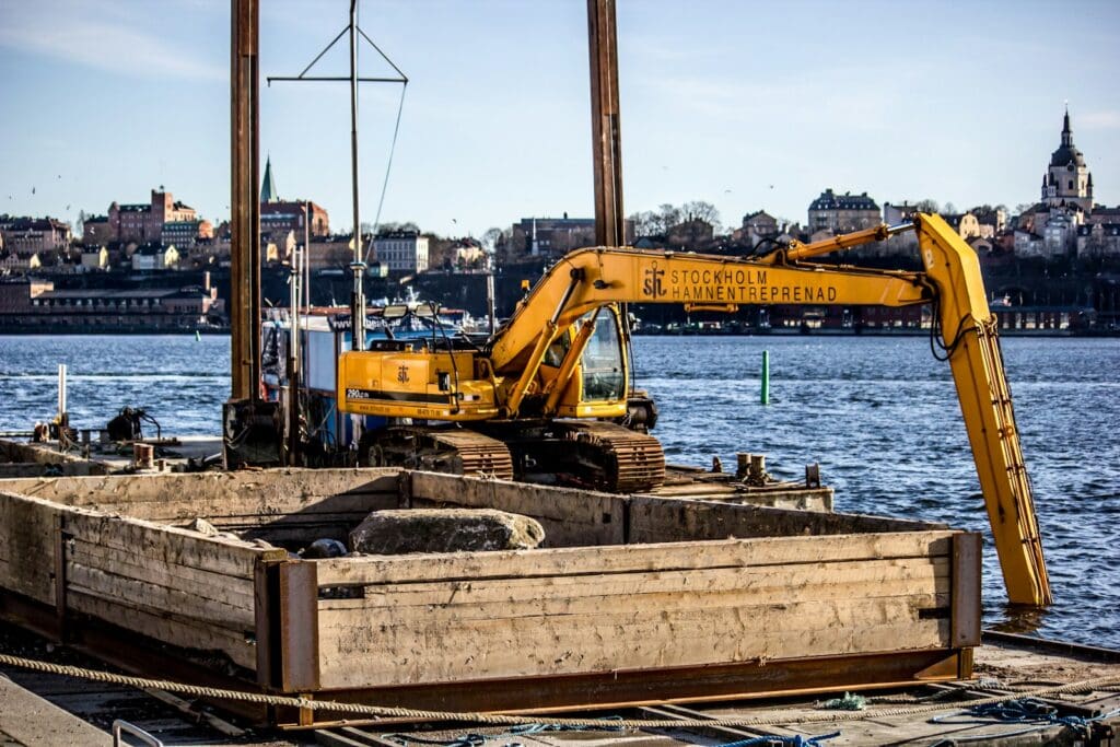 Construction Law 3 Yellow excavator on top of metal platform above sea. Dredging the river to install pilings. Construction Law. Legal Services