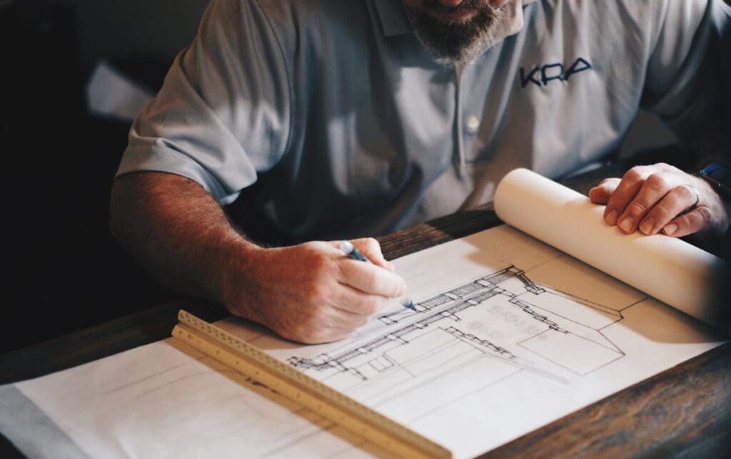 An architect working on a draft with a pencil and ruler. Design and construct vs Construct only