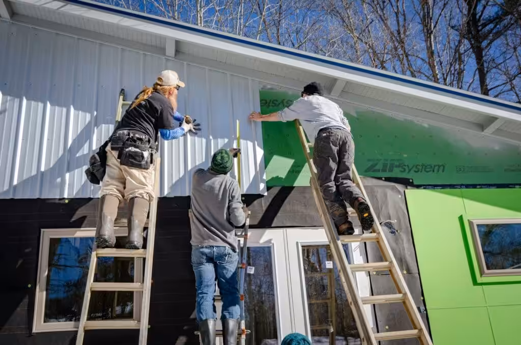Three tradesmen on ladders cladding a building. Small Business Management Consulting
