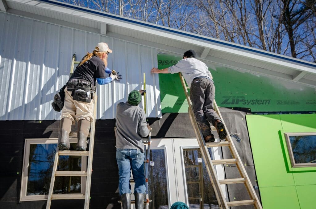 Transform Your Business in 2025 with our Small Business Management Consulting Services 4 Three tradesmen on ladders cladding a building. Small Business Management Consulting
