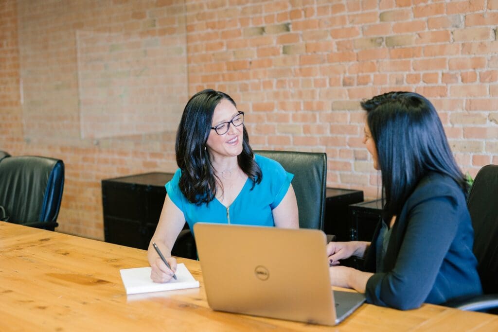 Woman in teal t-shirt sitting beside woman in suit jacket. Management Consulting and Strategy Consulting. Best Business Management Consultant Brisbane