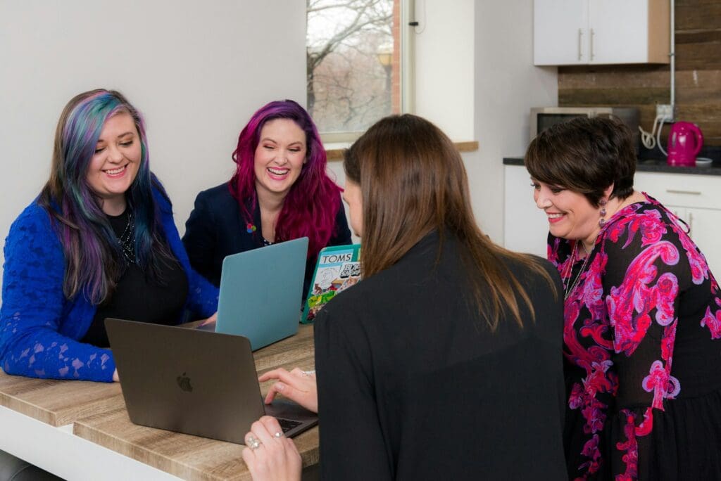 Transform Your Business in 2025 with our Small Business Management Consulting Services 8 Four woman on brown wooden table looking at laptops, consultants and clients doing Small Business Management Consulting