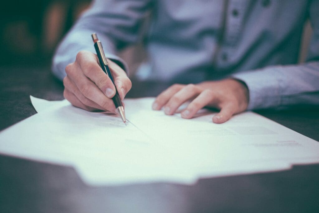 Business Loan Calculator - Should My Business Take Out A Loan? 1 Business Owner writing on paper loan documents. Business Loan Calculator