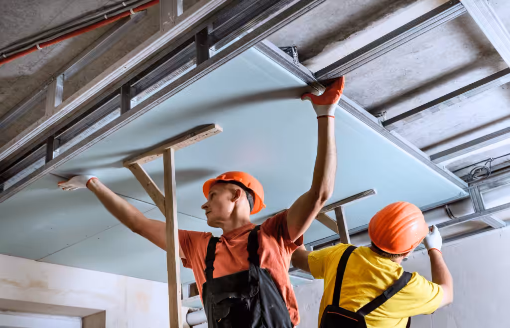 Two men in hard hats installing ceiling drywall. DLP Meaning