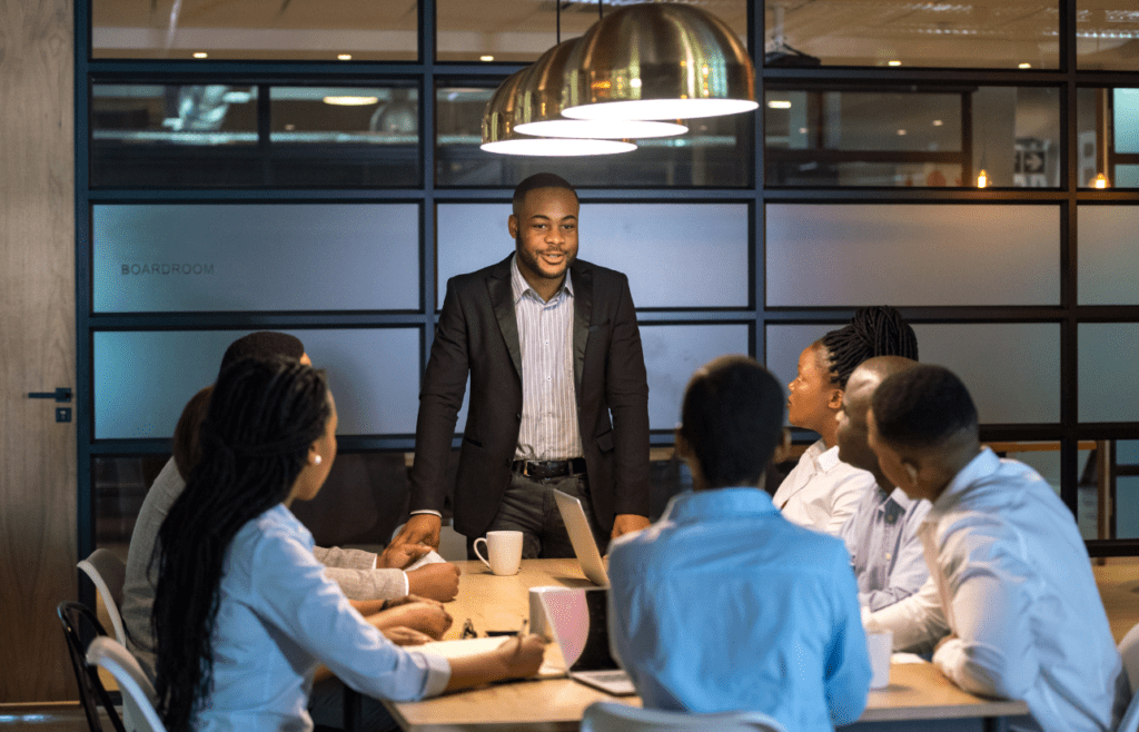 What is the Management Consulting Industry – A Practical Guide for Australian Businesses 16 A man stands before a group at a conference table. Managment Consulting Industry. Management Consulting Professional