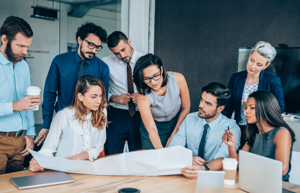 Discover Expert Management Consulting and Strategy Consulting 7 Group of businesspeople gathered around a table, reviewing a document. Management Consulting and Strategy Consulting. Management Consulting Professional