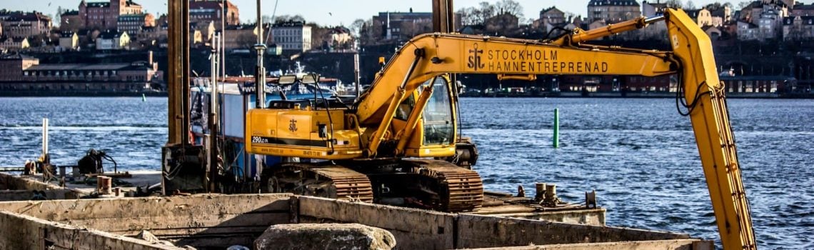 Yellow excavator on top of metal platform above sea. Australian Construction Law