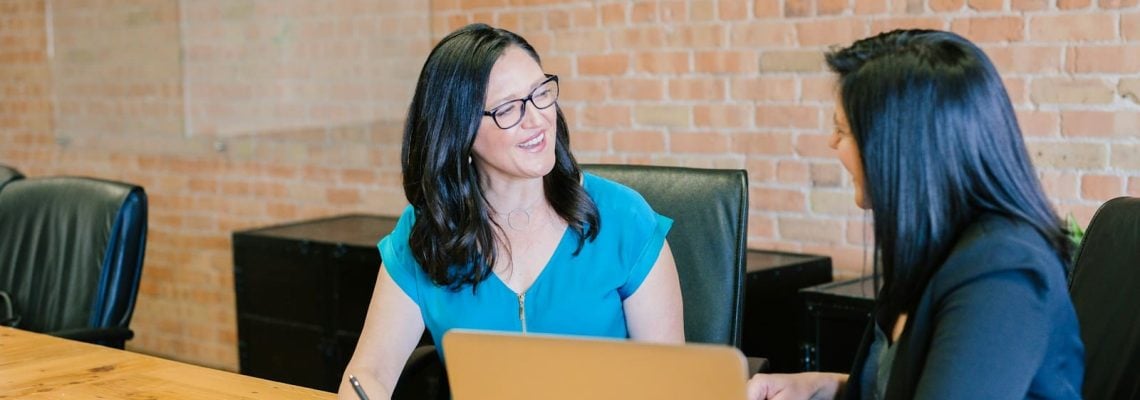 Woman in teal t-shirt sitting beside woman in suit jacket. Management Consulting and Strategy Consulting. Best Business Management Consultant Brisbane