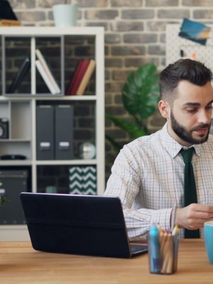 A man sitting at a desk in front of a laptop ensuring effective construction contract management.