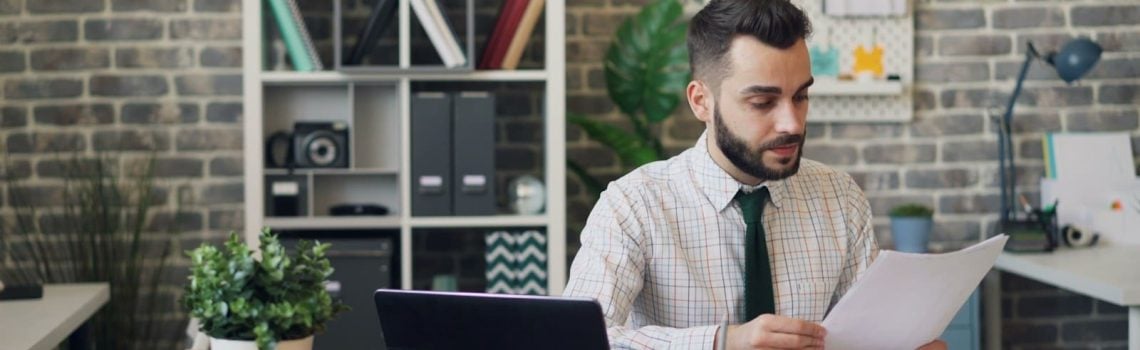 A man sitting at a desk in front of a laptop ensuring effective construction contract management.